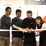 Four people cut a celebratory ribbon together, smiling, at an event backdrop with logos and a Playable Factory sign in the background.