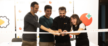 Four people cut a celebratory ribbon together, smiling, at an event backdrop with logos and a Playable Factory sign in the background.